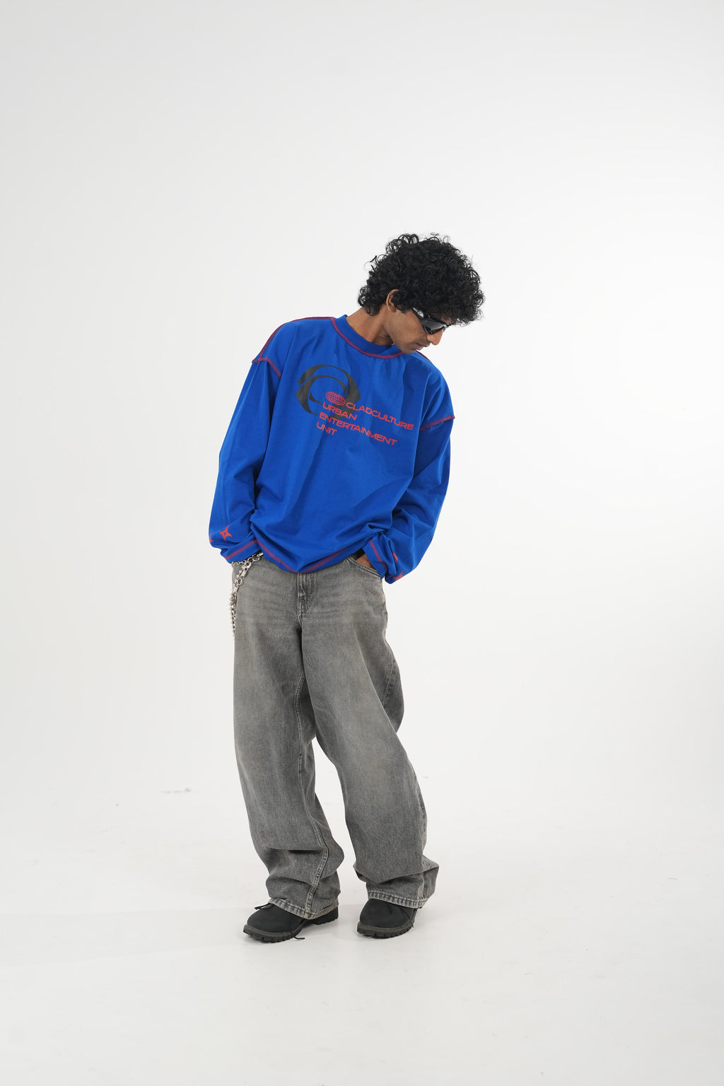 Model wearing a royal blue oversized long sleeve graphic T-shirt with contrast stitching and Urban Entertainment front print, paired with baggy grey jeans in a minimalist studio setting.
