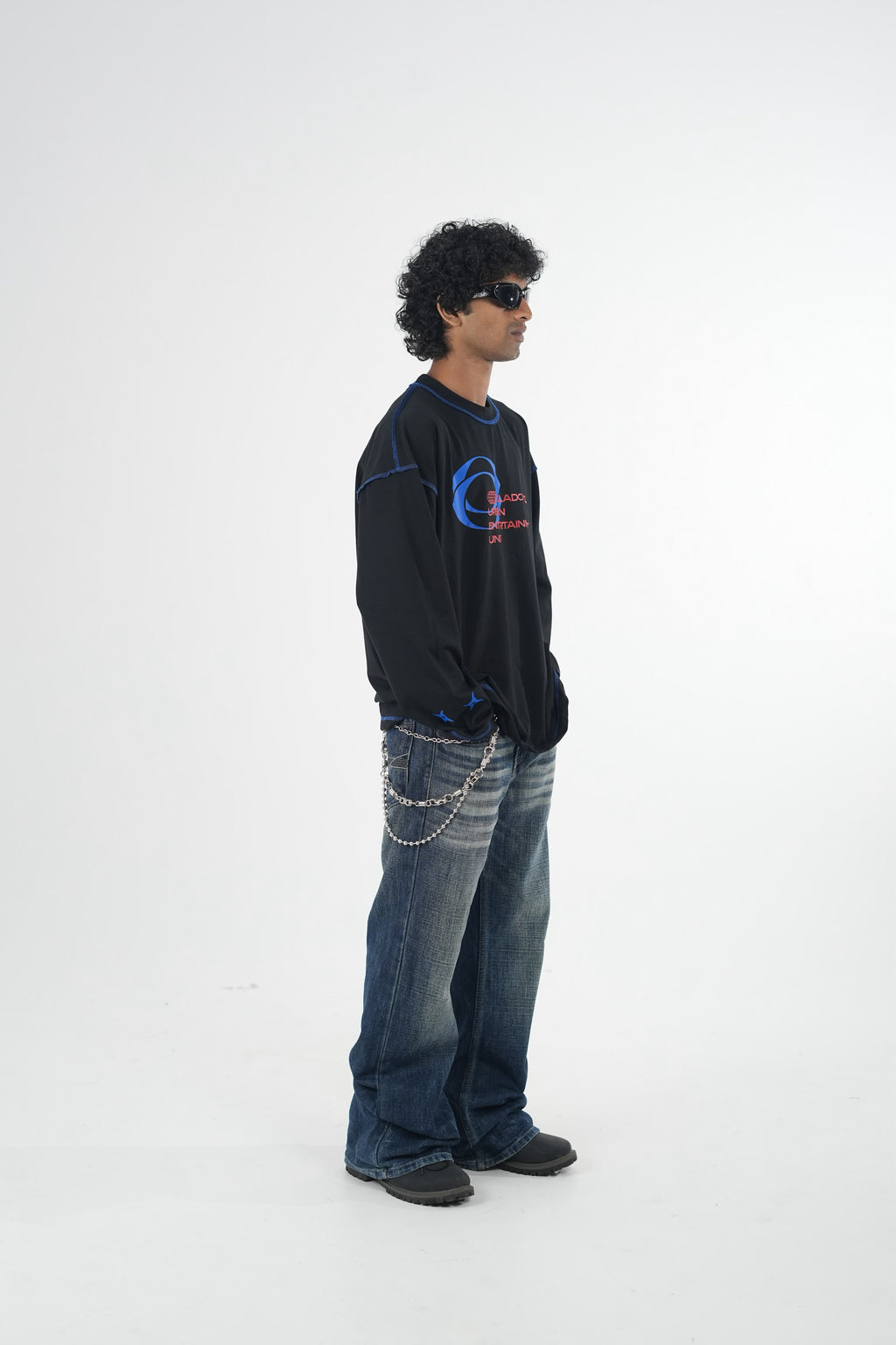 Model wearing a black oversized long sleeve graphic T-shirt with contrast stitching and Urban Entertainment front print, paired with baggy grey jeans in a minimalist studio setting.
