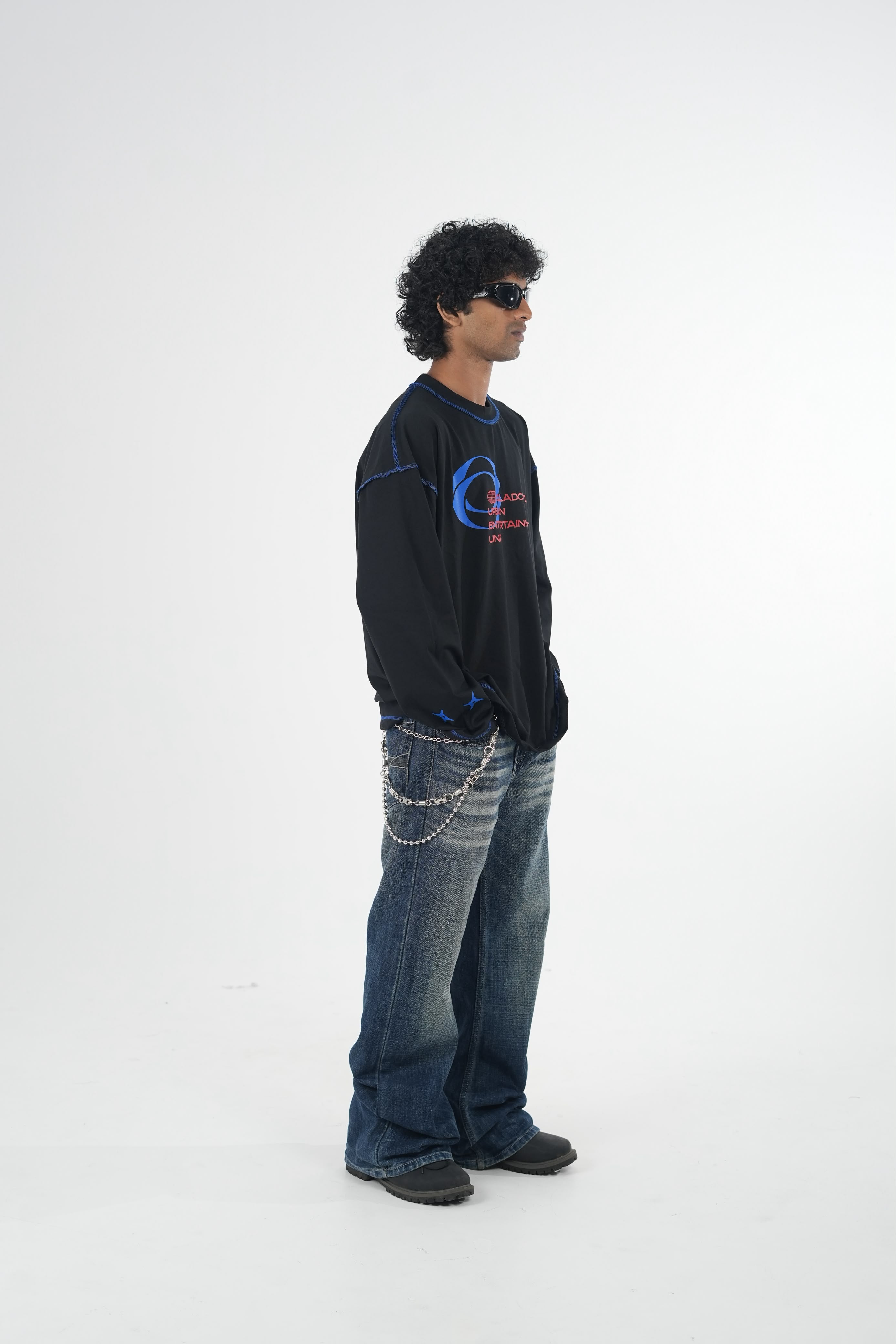 Model wearing a black oversized long sleeve graphic T-shirt with contrast stitching and Urban Entertainment front print, paired with baggy grey jeans in a minimalist studio setting.