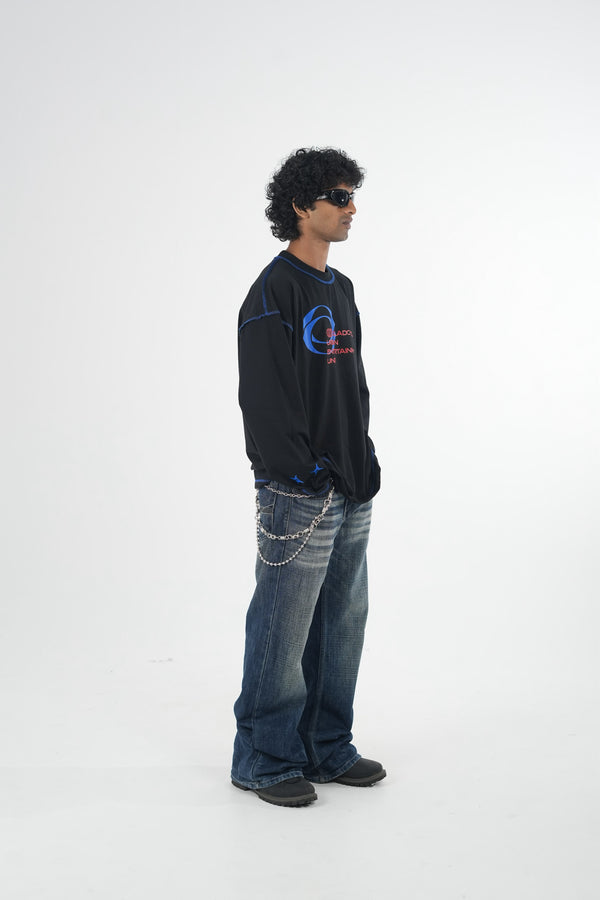Model wearing a black oversized long sleeve graphic T-shirt with contrast stitching and Urban Entertainment front print, paired with baggy grey jeans in a minimalist studio setting.