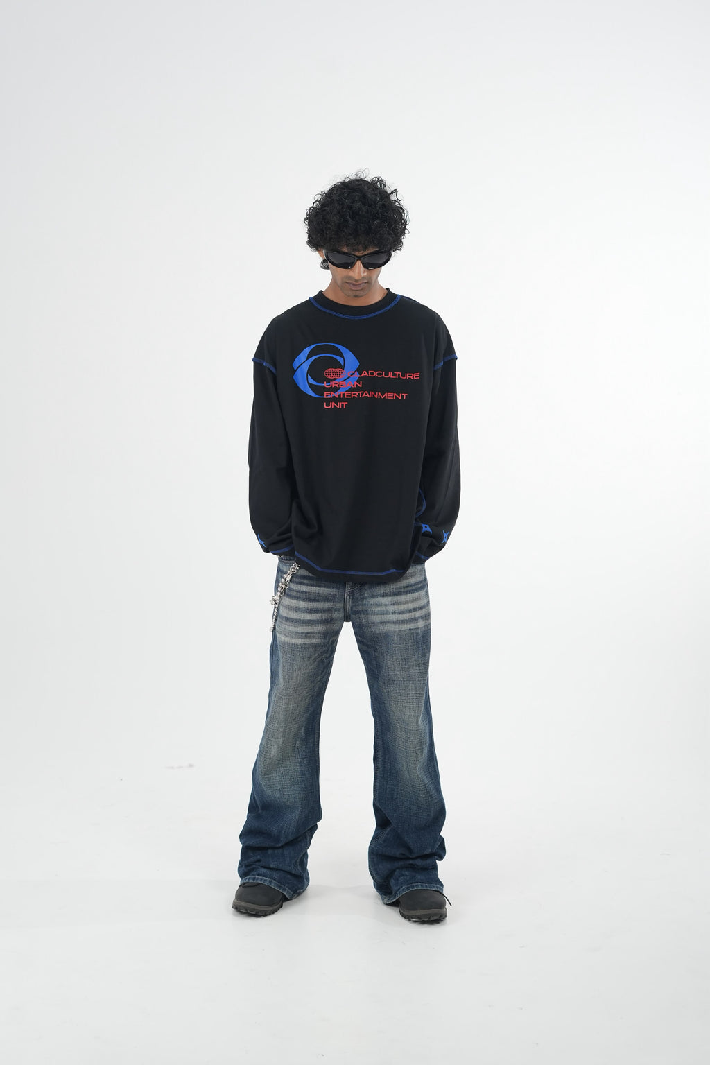 Model wearing a grey oversized long sleeve graphic T-shirt with contrast stitching and Urban Entertainment front print, paired with baggy grey jeans in a minimalist studio setting.