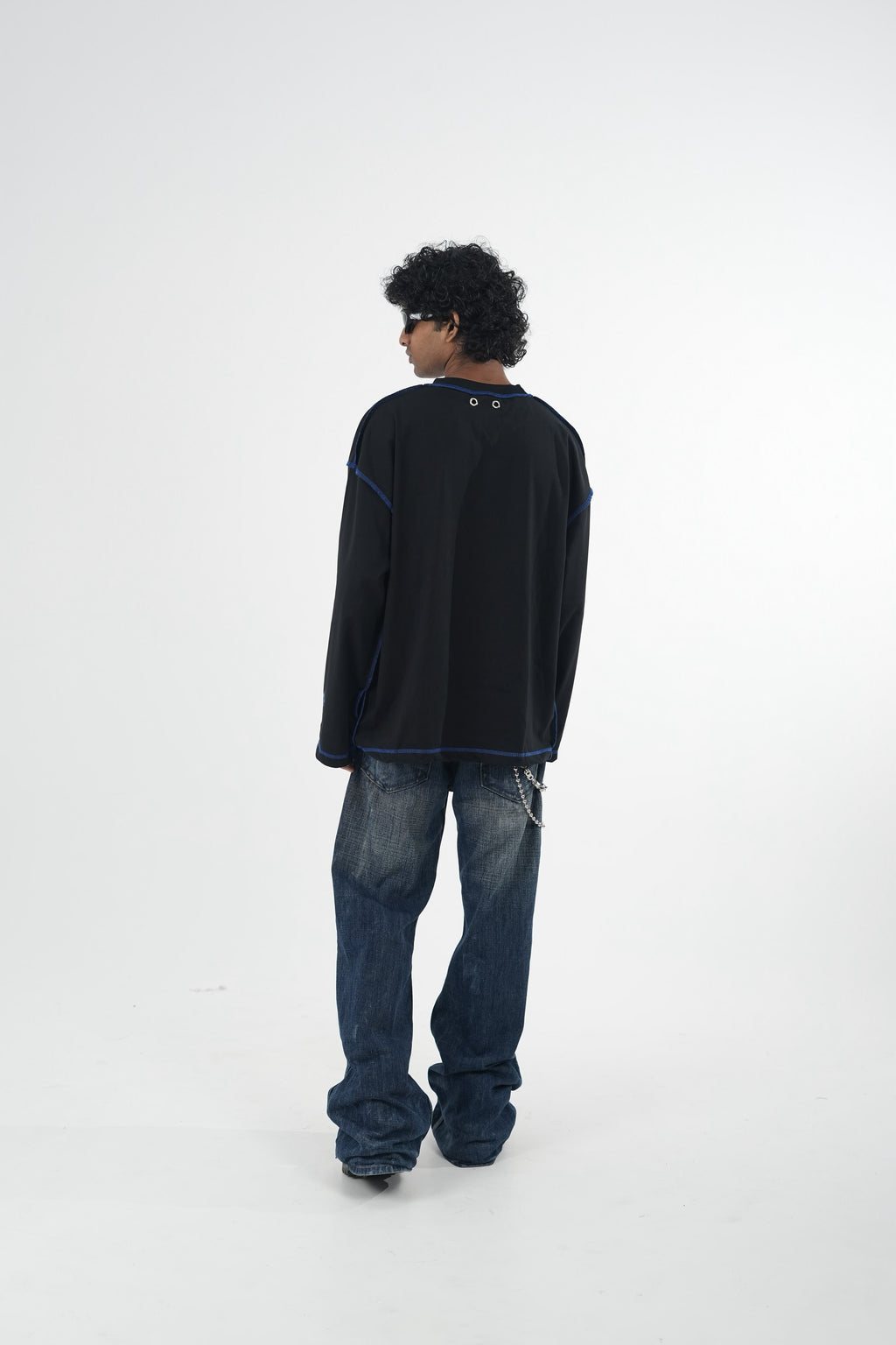 Model wearing a black oversized long sleeve graphic T-shirt with contrast stitching and Urban Entertainment front print, paired with baggy grey jeans in a minimalist studio setting.