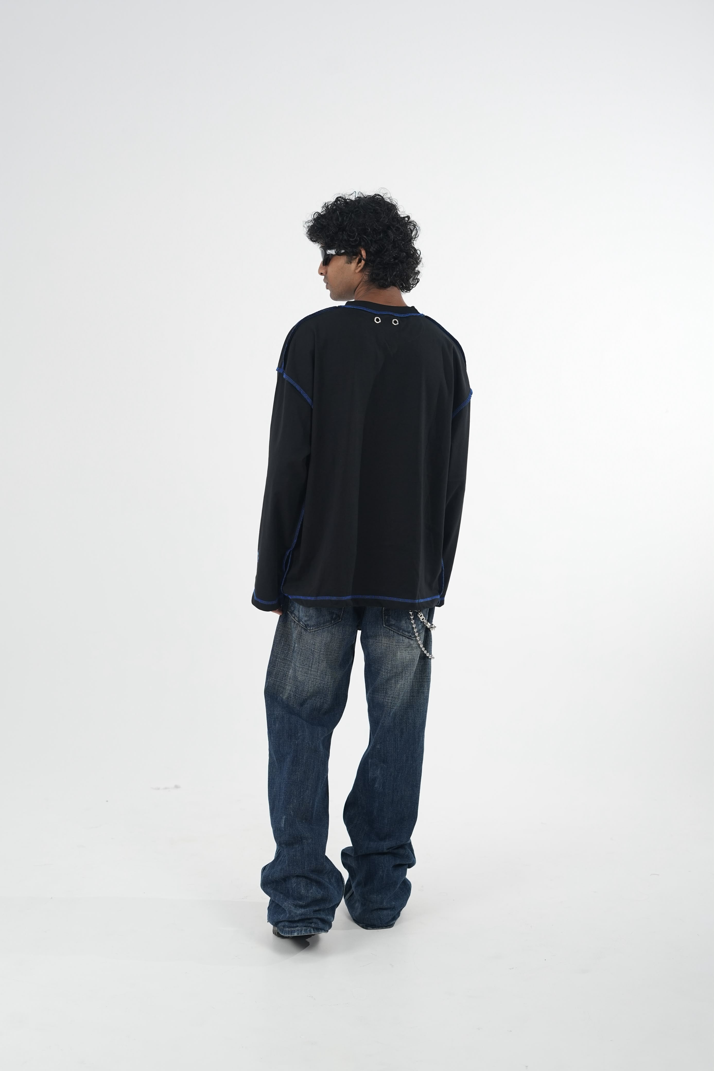 Model wearing a black oversized long sleeve graphic T-shirt with contrast stitching and Urban Entertainment front print, paired with baggy grey jeans in a minimalist studio setting.