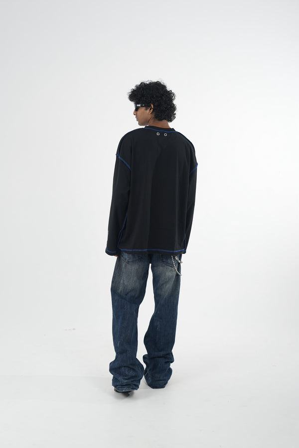 Model wearing a black oversized long sleeve graphic T-shirt with contrast stitching and Urban Entertainment front print, paired with baggy grey jeans in a minimalist studio setting.