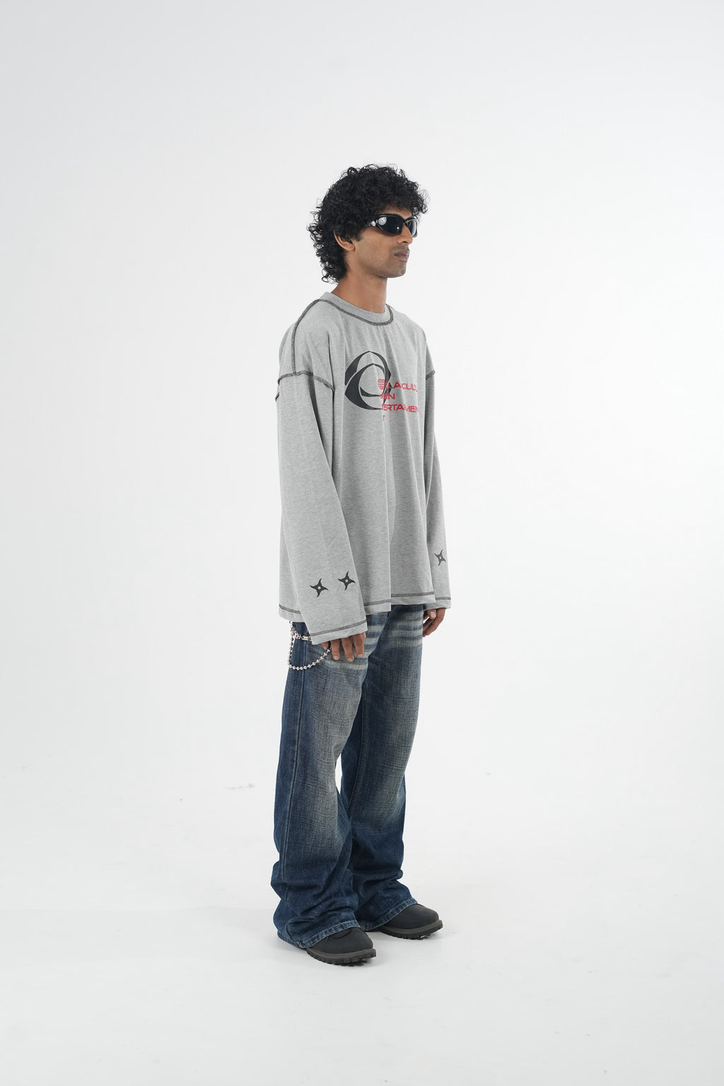 Model wearing a grey oversized long sleeve graphic T-shirt with contrast stitching and Urban Entertainment front print, paired with baggy grey jeans in a minimalist studio setting.