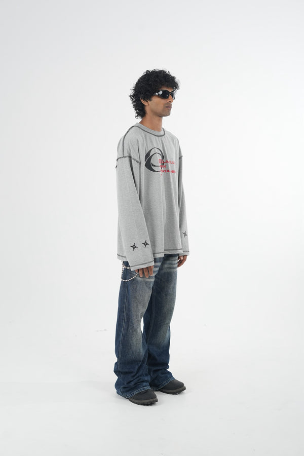 Model wearing a grey oversized long sleeve graphic T-shirt with contrast stitching and Urban Entertainment front print, paired with baggy grey jeans in a minimalist studio setting.