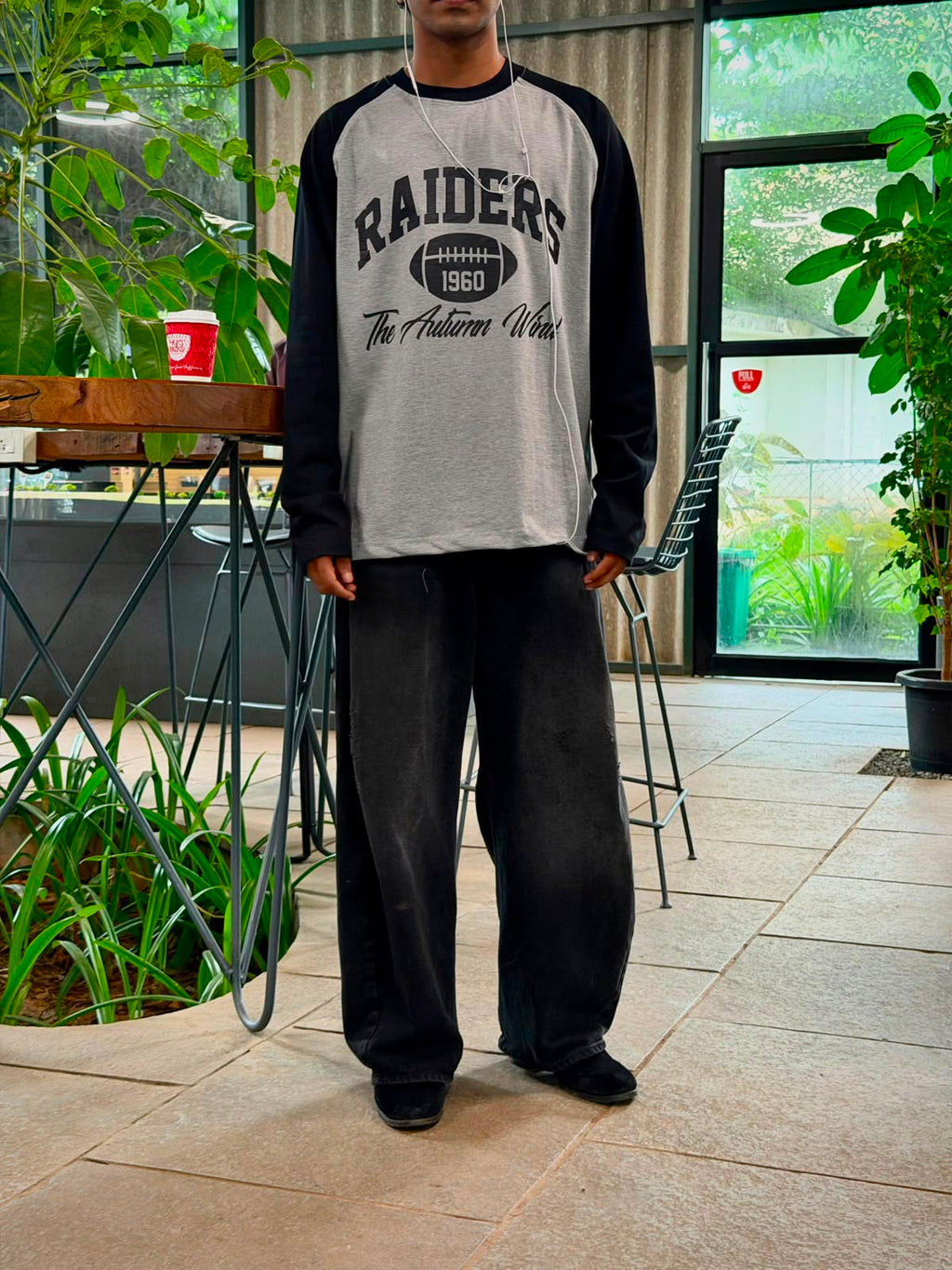 Model wearing a vintage oversized grey and black  Raiders raglan full sleeve graphic T-shirt