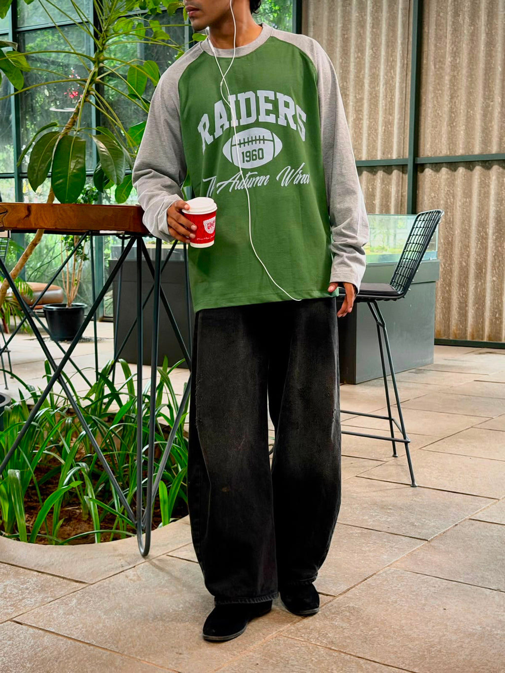 Model wearing a vintage oversized grey and green Raiders raglan full sleeve graphic T-shirt