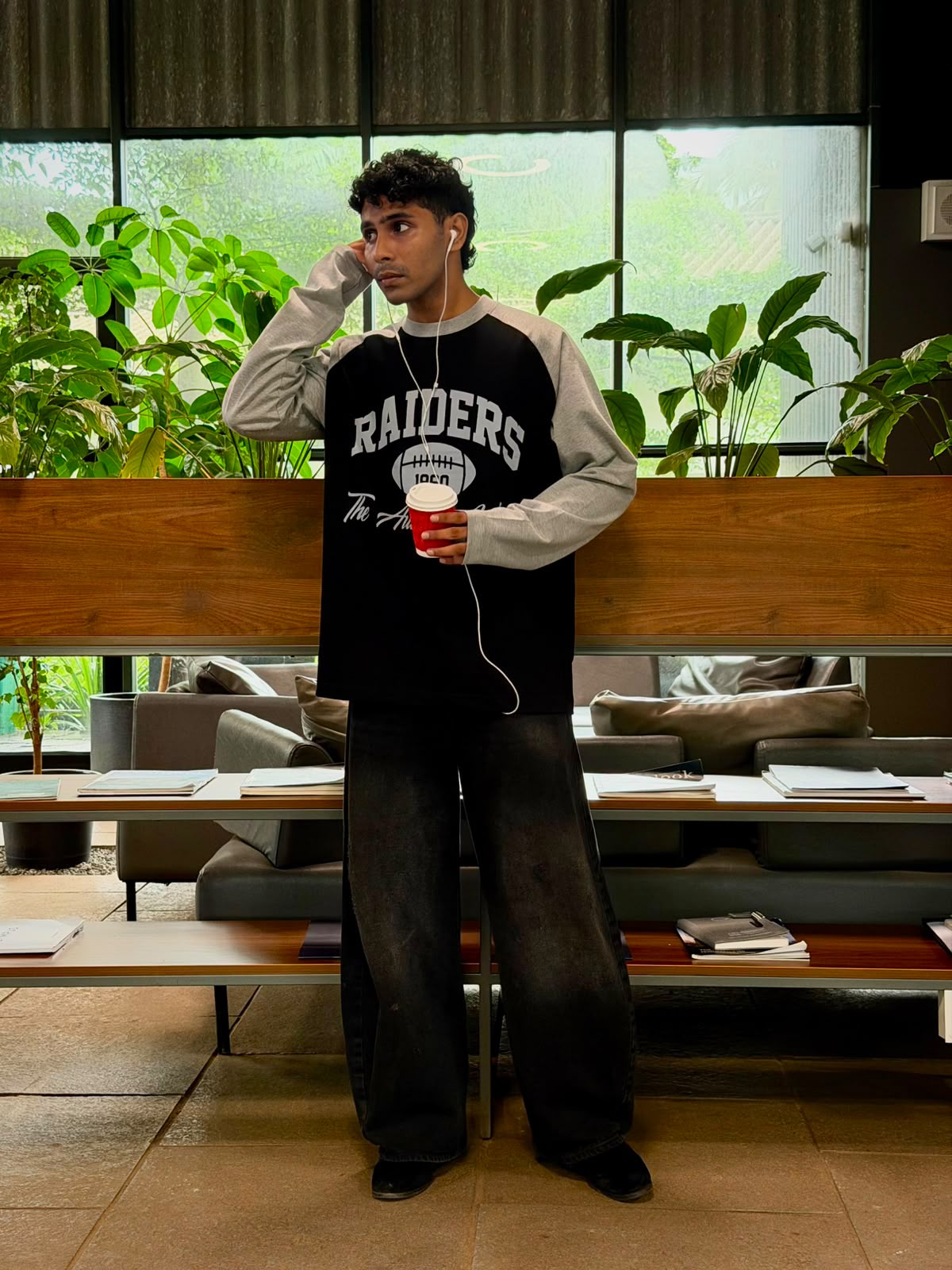 Model wearing a vintage oversized grey and black  Raiders raglan full sleeve graphic T-shirt
