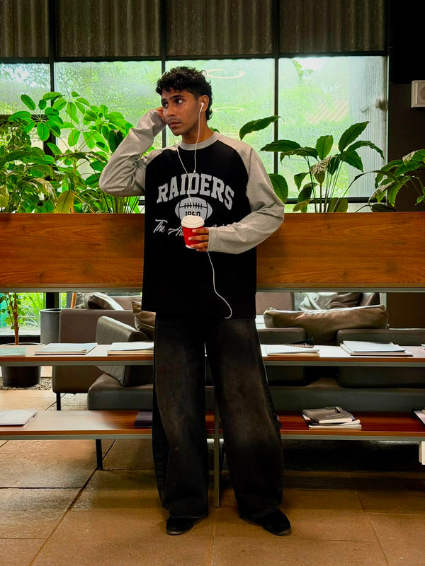 Model wearing a vintage oversized grey and black  Raiders raglan full sleeve graphic T-shirt